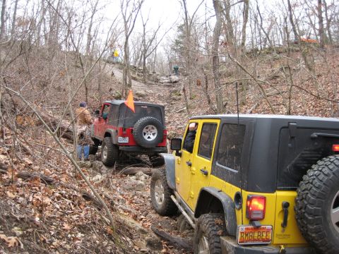 2005 Jeep Wrangler - Two Jeep Wranglers navigate a challenging off-road trail through a wooded area.