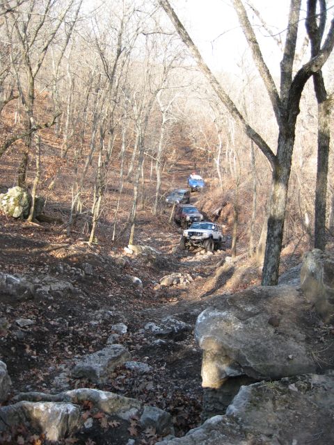 2005 Jeep Wrangler - A line of lifted 4x4s, a white Jeep Cherokee XJ on oversized tires in front, followed by red, dark and blue rigs, descending a rocky, rutte…