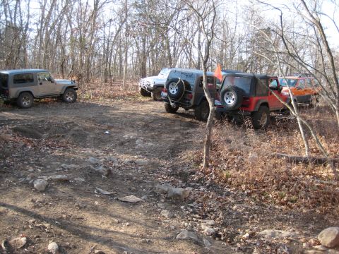 2005 Jeep Wrangler - Multiple Jeep Wranglers are parked on a dirt path surrounded by trees in a wooded area.