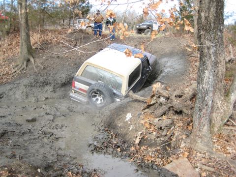 2005 Jeep Wrangler - An off-road vehicle navigates a muddy terrain, with other vehicles and people visible in the background.