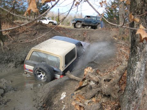 2005 Jeep Wrangler - Multiple off-road vehicles struggle through a muddy trail, with one vehicle stuck in a deep ditch.
