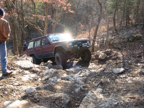 2005 Jeep Wrangler - A maroon Jeep Cherokee XJ is shown off-roading on a challenging, rocky path.