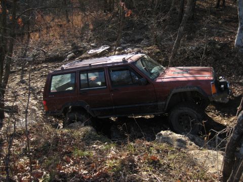 2005 Jeep Wrangler - A red Jeep Cherokee XJ navigates a challenging off-road trail with steep inclines and rocky terrain.