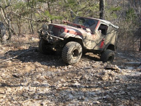 2005 Jeep Wrangler - A red Jeep Wrangler navigates a challenging rocky terrain in a wooded area.