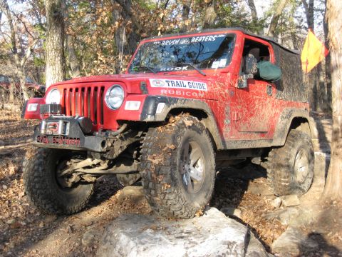 2005 Jeep Wrangler - A red Jeep Wrangler navigates a rocky trail, its tires covered in mud and leaves.