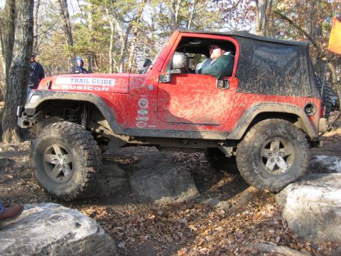 2005 Jeep Wrangler - A red 2005 Jeep Wrangler Rubicon navigates a rocky trail, its body splattered with mud.