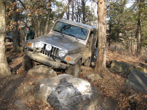 2005 Jeep Wrangler - A Jeep Wrangler is shown navigating a rocky trail in a wooded area, with another vehicle partially visible in the background.