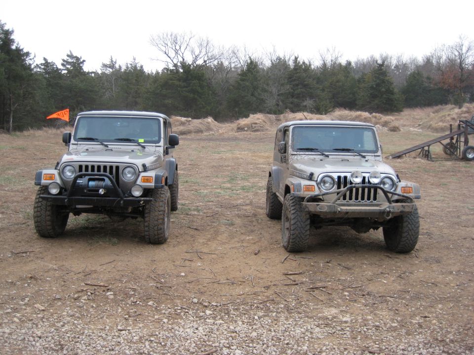 Two 2005 Jeep Wranglers parked on dirt with trees in the background