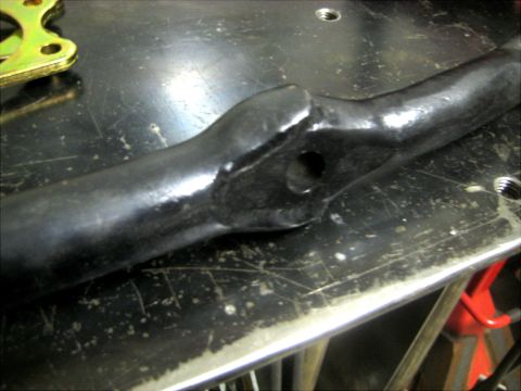 1996 Ford Bronco - Close-up of a black metal suspension component with a hole, on a workbench.