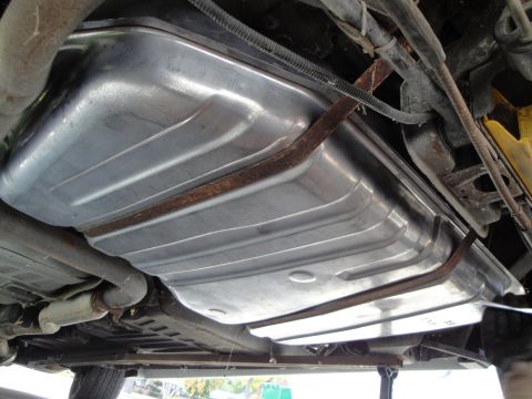 1995 Ford Taurus - Underside view of a silver fuel tank with ribbed texture, held by rusty straps.