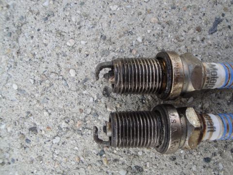 1995 Ford Taurus - Two used Motorcraft spark plugs are shown on a concrete surface, indicating wear on their electrodes.