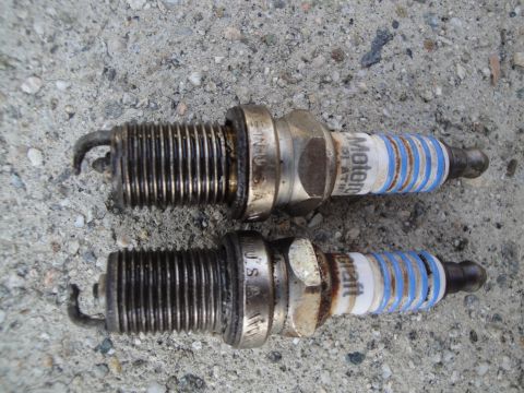1995 Ford Taurus - Two used Motorcraft spark plugs are shown resting on a concrete surface, indicating they are a vehicle part.