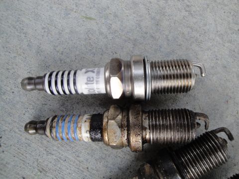 1995 Ford Taurus - Two spark plugs are shown, one clean and one dirty, on a concrete surface.