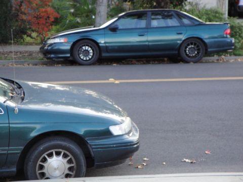 1995 Ford Taurus - A green sedan is parked on the side of the road, with another car partially visible in the foreground.