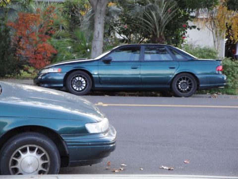 1995 Ford Taurus - A green sedan is parked on the side of the road, with another car partially visible in the foreground.