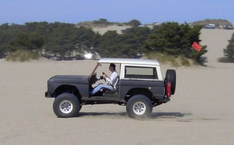 1980 Ford Bronco - Ford Bronco navigates sandy terrain under a clear sky.
