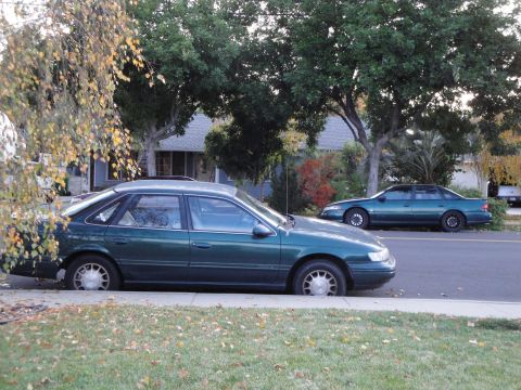 1995 Ford Taurus - A 1995 Ford Taurus sedan is parked on a residential street next to another green sedan.
