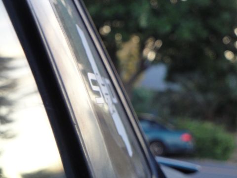 1995 Ford Taurus - A close-up of car window trim with a white sticker, with a blurred car visible in the background.
