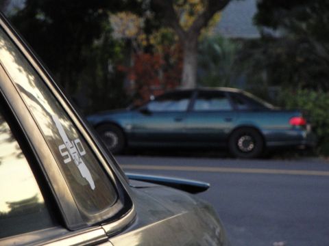 1995 Ford Taurus - A 1995 Ford Taurus SHO is seen parked on the side of the road, with a portion of another vehicle in the foreground.