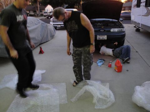 1995 Ford Taurus - Mechanics work on a 1995 Ford Taurus in a driveway with the hood up.