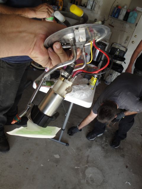 1995 Ford Taurus - A person holds a fuel pump assembly with a filter and wiring, while another person works nearby.