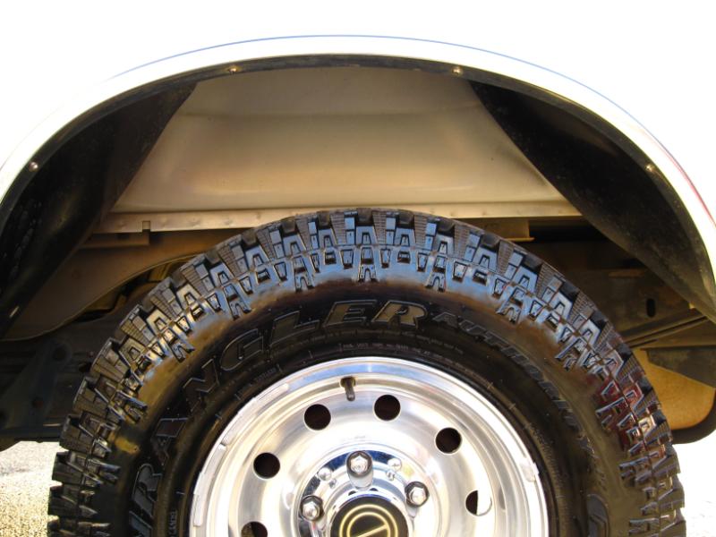 Close-up of a tire and wheel well on a vehicle. The tire is a Goodyear Wrangler. The wheel is chrome with five lug nuts