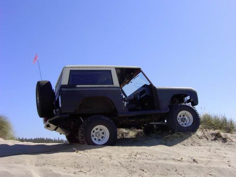 1980 Ford Bronco - A dark gray 1978 Ford Bronco with a white top is parked on a sand dune under a clear blue sky.