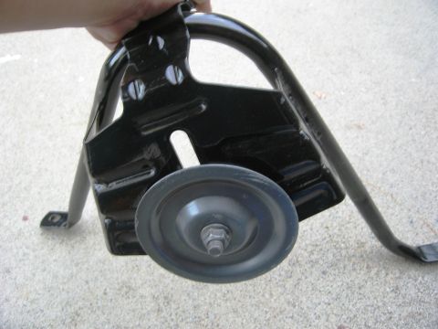 1986 Ford Bronco - A black metal bracket, likely for a tire carrier, is held up, showing its roller wheel and mounting points.