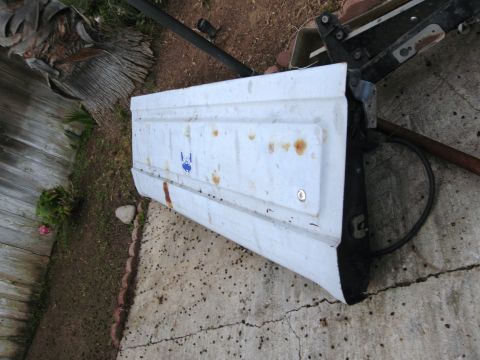 1986 Ford Bronco - A white tailgate with a blue emblem is shown outdoors, resting on a cracked concrete surface.