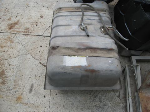 1986 Ford Bronco - A used vehicle gas tank is shown, resting on a cracked concrete surface with some metal framing nearby.