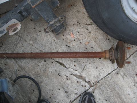 1986 Ford Bronco - A single, rusty axle shaft is visible on a cracked concrete ground, with a tire and part of a trailer frame in the background.
