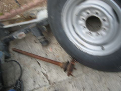 1986 Ford Bronco - A rusty axle part lies on the ground next to a vehicle tire.