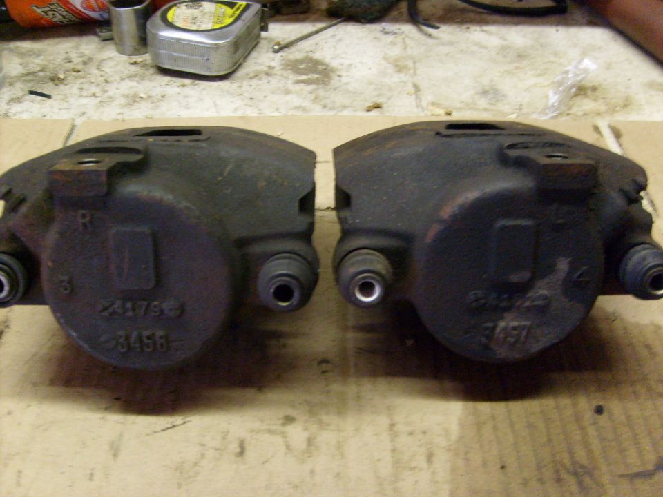 Two brake calipers sitting on a workbench, one on the left and one on the right