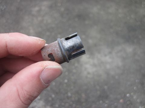 1979 Ford Bronco - A close-up view of a small metal and plastic automotive part being held by a person's fingers.