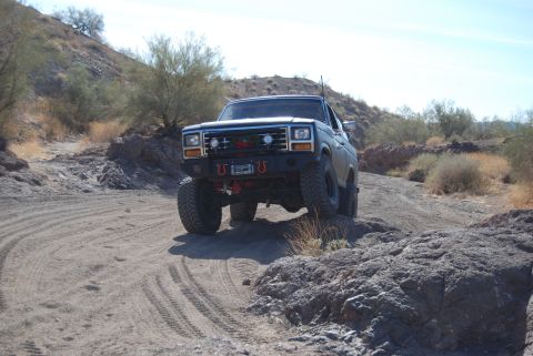 1982 Ford Bronco - This heavily modified pickup truck navigates a challenging off-road path in a desert landscape.