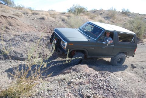 1982 Ford Bronco - A man drives a dark gray Ford Bronco off-road on a sunny day.