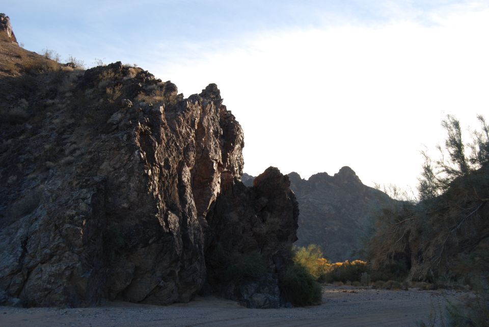 Rocky desert terrain under a bright sky, with scrub brush and distant mountains