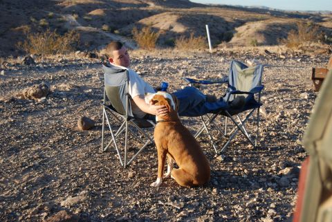 1982 Ford Bronco - Man and dog relax in camping chairs in a rocky desert environment.