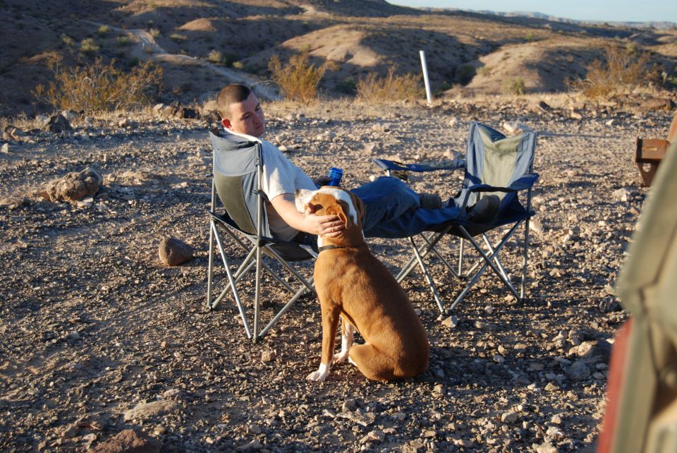 Man petting dog while sitting in camping chairs in a desert landscape