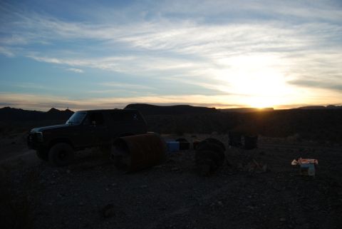 1982 Ford Bronco - A Ford Bronco sits in a desolate area as the sun sets behind distant hills.