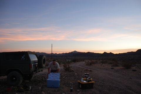 1982 Ford Bronco - A man prepares supplies next to a Ford Bronco in a desert setting as the sun sets.