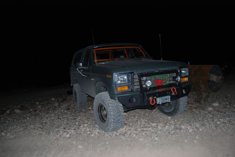 Dark green Ford Bronco with aftermarket bumper and winch, parked on gravel at night