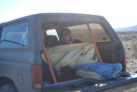 1982 Ford Bronco - A person is seen inside a Ford Bronco, surrounded by blankets and a roll cage, in an outdoor setting.
