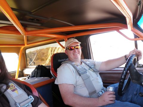 1982 Ford Bronco - Driver and passenger inside a modified vehicle with an orange roll cage and racing harnesses, ready for off-road adventure.