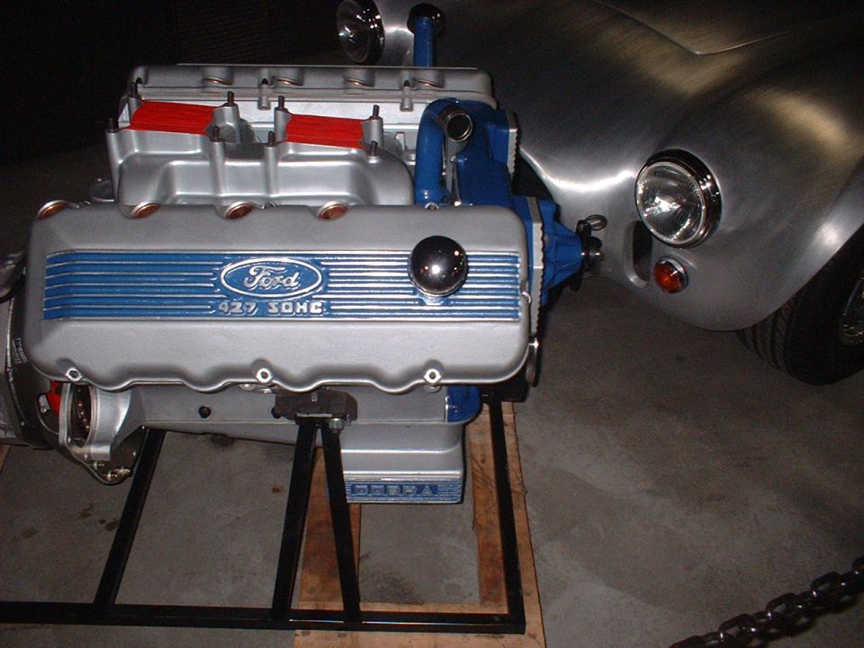 Ford 427 SOHC Cammer V8 engine on stand beside a silver Cobra roadster body