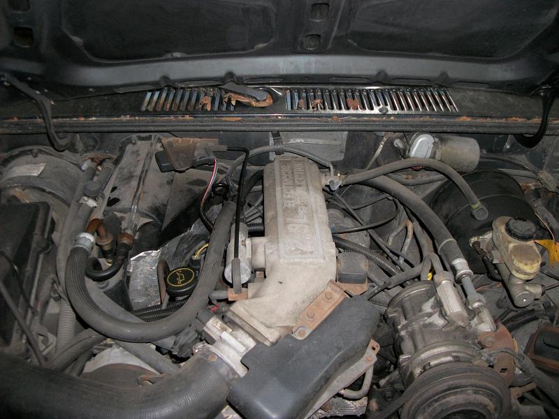 Engine bay with hoses, wires, and engine components visible. Text on engine reads 'Ford-Mazda'