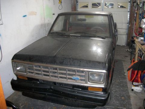 1987 Ford Ranger - A dusty black 1987 Ford Ranger truck is parked head-on in a garage.
