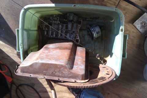 1987 Ford Bronco - Various rusty transmission components are stored in a plastic tub on a wooden surface.