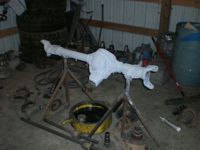 Differential axle assembly covered in white protective wrap, resting on stands in a garage