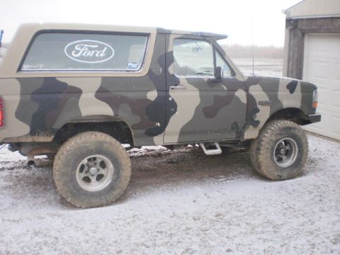 1995 Ford Bronco - Camouflaged 1995 Ford Bronco parked outside a garage in snowy conditions.